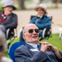 Focus on gentleman sitting in lawn chair smiling while other event attendees are out of focus